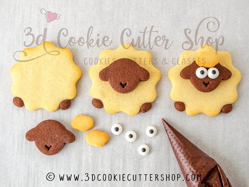 May include: Three decorated sugar cookies shaped like sheep. The cookies are decorated with brown and yellow icing and white candy eyes. The cookies are on a white surface. The image also shows a piping bag with brown icing and additional cookie pieces.