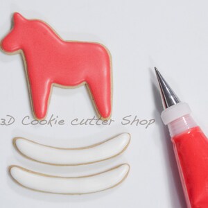 May include: A red Dala horse cookie with a tan border sits above two white cookies with tan borders. A pastry bag filled with red icing and a metal tip is in the image. The text "&copy;3D Cookie cutter Shop" is in the image.
