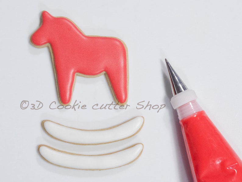 May include: A red Dala horse cookie with a tan border sits above two white cookies with tan borders. A pastry bag filled with red icing and a metal tip is in the image. The text "&copy;3D Cookie cutter Shop" is in the image.