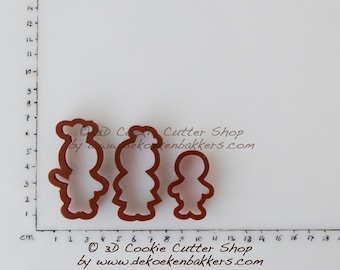 May include: Three brown cookie cutters shaped like people. The cutters are arranged in a row from left to right, with the largest cutter on the left and the smallest cutter on the right. The cutters are on a white surface with a ruler marked in centimeters.