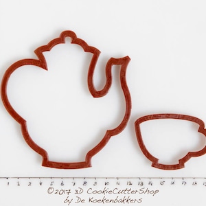 Könnte beinhalten: Ein brauner Plastik-Ausstecher in Form einer Teekanne und einer passenden Tasse. Die Ausstecher befinden sich auf einer weißen Oberfläche mit einem Lineal in Zentimetern.