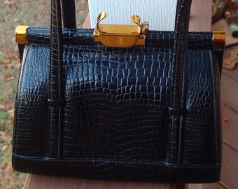 May include: A black crocodile-embossed handbag with gold-tone hardware and a top handle.