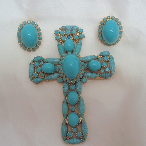May include: A turquoise blue cross pendant with matching earrings. The cross is made of gold-toned metal and is adorned with turquoise blue stones.