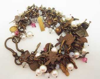 May include: A gold charm bracelet featuring a range of charms, including keys, butterflies, hearts, and a charm that reads "Love". The bracelet is also adorned with white pearls and pink beads.