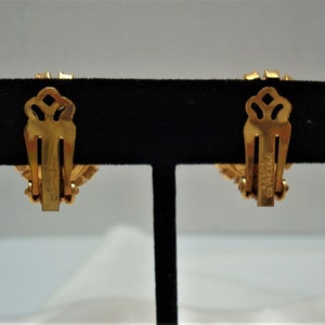 May include: A pair of gold-tone clip-on earrings with a floral design. The earrings have a "Coro" signature on the back.