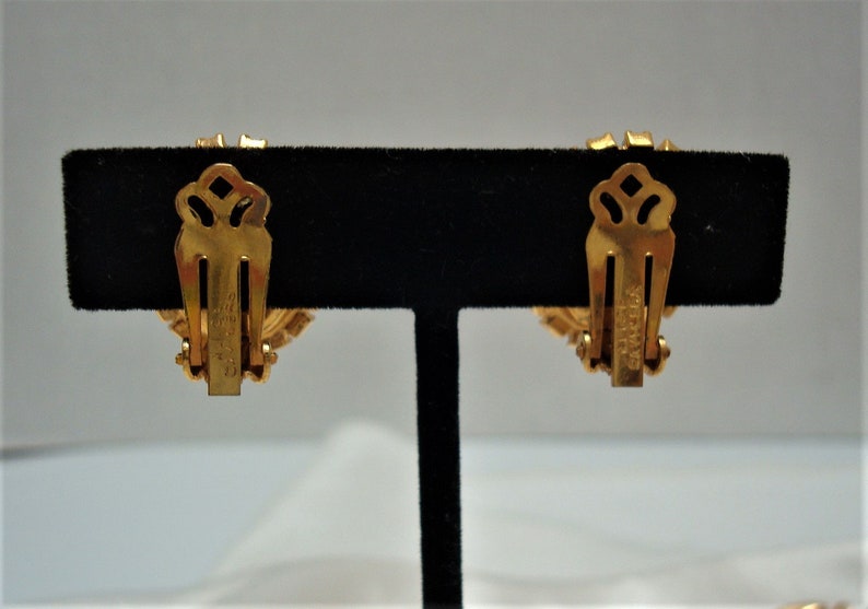 May include: A pair of gold-tone clip-on earrings with a floral design. The earrings have a "Coro" signature on the back.