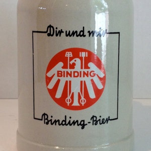 May include: A white ceramic beer stein with a red and white logo that says "Binding" and the text "Dir und mir Binding-Bier".