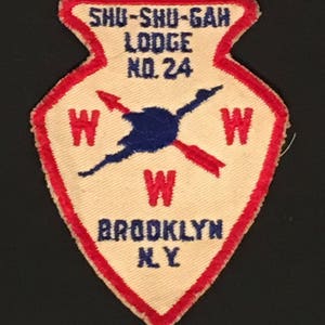 May include: White and red arrowhead-shaped patch with blue embroidered text "Shu-Shu-Gah Lodge No. 24" and "Brooklyn NY". The patch also features a blue and red embroidered compass with the letter "W" in each direction.