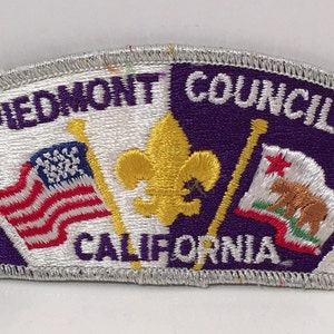 Puede incluir: Parche bordado morado y blanco con el texto "Piedmont Council California" e imágenes de la bandera estadounidense, una flor de lis y la bandera del estado de California.
