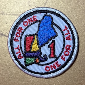 以下が含まれることがあります： カラフルな州の地図と「All for One One for All」というテキストが書かれた白い刺繍パッチです。