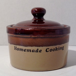 May include: A brown and tan ceramic jar with a lid. The jar has the words "Homemade Cooking" written on the front.