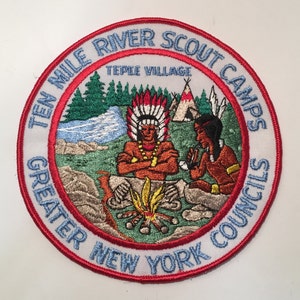 May include: A white embroidered patch with a red border. The patch features a scene of two Native American figures sitting by a campfire in a forest setting. The text on the patch reads "Ten Mile River Scout Camps Greater New York Councils Teepee Village".