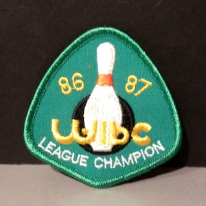May include: Green felt patch with a white bowling pin and a black and gold bowling ball. The text "WIBC LEAGUE CHAMPION" is written in gold letters. The numbers "86" and "87" are written in gold on either side of the bowling pin.
