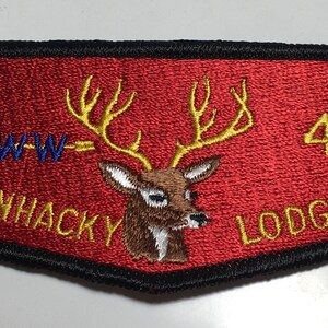Könnte beinhalten: Ein roter gestickter Aufnäher mit einem goldenen Hirschkopf und Geweih, der Text "WWW-SUANHACKY LODGE-49" in goldenen Buchstaben.