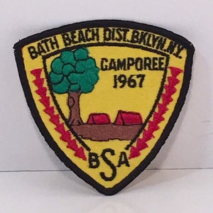 Könnte beinhalten: Gelber dreieckiger Patch mit schwarzem Rand, roten und weißen Blitzen, einem grünen Baum, zwei roten Zelten und dem Text "Bath Beach Dist. Brooklyn, NY. Camporee 1967 BSA".