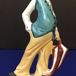 Peut inclure: Une figurine en porcelaine d'un clown avec un gilet bleu, un pantalon jaune et un parapluie brun et blanc. Le clown porte un chapeau blanc avec une bande noire.