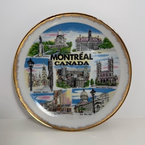 Puede incluir: Un plato de recuerdo redondo de cerámica blanca con borde dorado que presenta un collage de monumentos de Montreal, Canadá, incluidos el Oratorio de San José, el Ayuntamiento, Notre Dame y la Rue Ste-Catherine, con el texto Montréal Canada en el centro.
