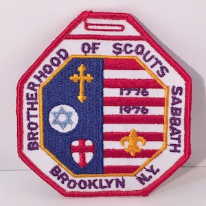 May include: A white octagonal patch with red embroidered border. The patch features the text "Brotherhood of Scouts Sabbath Brooklyn NY" in a purple and gold circular design. The center of the patch features a blue and white American flag with a red, white, and blue cross, a gold Star of David, and a gold fleur-de-lis. The flag has the years "1776" and "1976" embroidered on it.