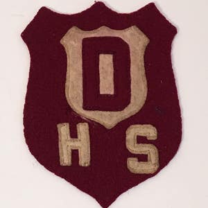 May include: A maroon felt patch with a white felt letter "O" inside a white felt shield. Below the shield are the letters "HS" in white felt.