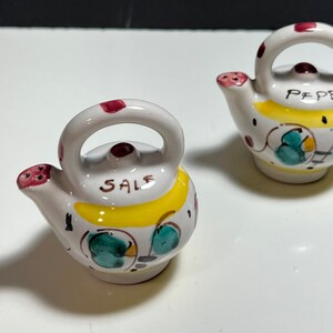 May include: Two small ceramic teapots, one labeled "SALE" and the other "PEPE", with yellow, green, and red painted designs.