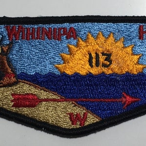 Puede incluir: Un parche bordado azul y dorado con el texto "WINNIPPA" y "HINSA" y el número "113". El parche presenta una tienda de campaña, un sol naciente y una flecha apuntando hacia la derecha.