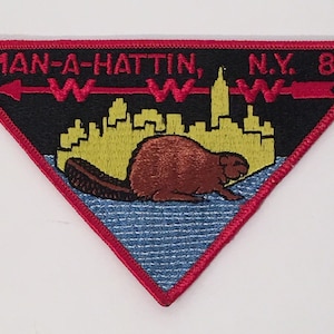 May include: A triangular embroidered patch with a red border. The patch features a black background with a cityscape, a beaver, and the text "MAN-A-HATTIN, N.Y. 82".