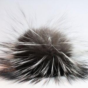 Könnte beinhalten: Ein flauschiger schwarz-weißer Pelzbommel. Der Bommel besteht aus weichem, luxuriösem Fell und ist perfekt, um jedem Hut oder Accessoire einen Hauch von Stil zu verleihen.