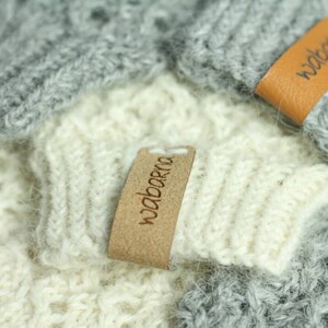 May include: Two knitted hats with brown leather labels that say "wabarna". The hats are one gray and one white.