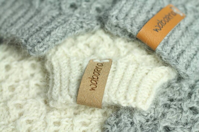 May include: Two knitted hats with brown leather labels that say "wabarna". The hats are one gray and one white.