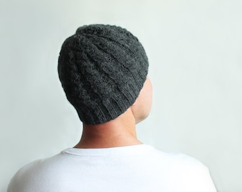 Puede incluir: Un gorro de punto gris oscuro con un patrón de trenza.