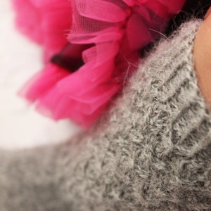 May include: A close-up of a gray knitted sock with a pink tulle fabric in the background.