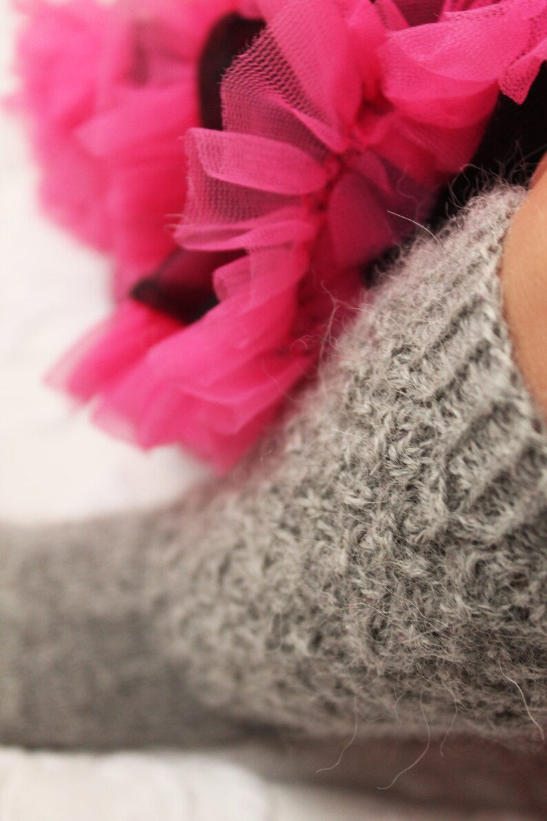 May include: A close-up of a gray knitted sock with a pink tulle fabric in the background.