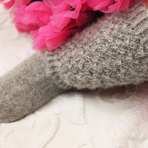 May include: A close-up of a gray knitted sock with a fuzzy texture. The sock is worn by a person and is partially covered by a pink tulle skirt.