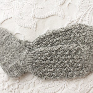 May include: A pair of gray knitted socks with a textured pattern. The socks are folded and lying on a white textured surface.