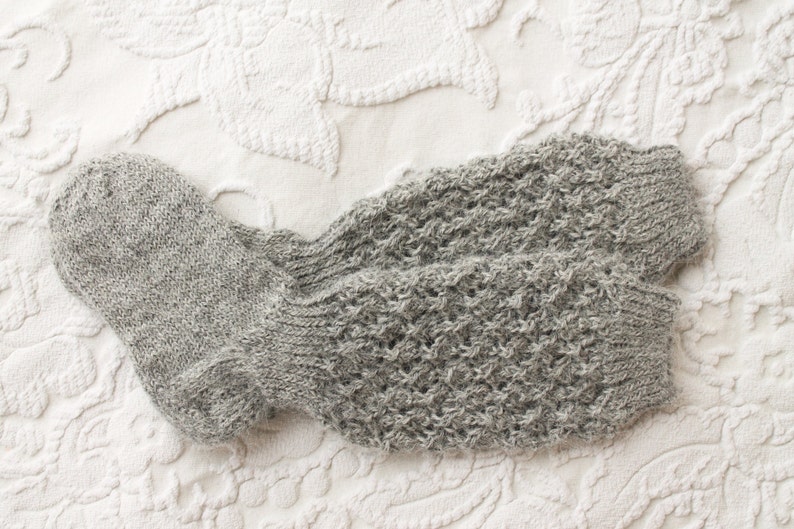 May include: A pair of gray knitted socks with a textured pattern. The socks are folded and lying on a white textured surface.