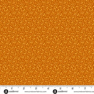 May include: Close-up of a fabric with a repeating pattern of small, light yellow leaf-like shapes on a dark orange background. The fabric has a dense, all-over design. A ruler is at the bottom of the image.