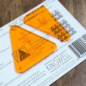May include: Two orange plastic quilting templates for making a 60 degree triangle quilt block. The templates are labeled "Not Quite 60 Degree Triangle" and "Jen Kingwell Designs".