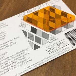 May include: A clear orange plastic template for a diamond-shaped quilt block. The template is labeled "half template top & bottom" and is part of the "Postcard Project #2" series by Jen Kingwell Designs.