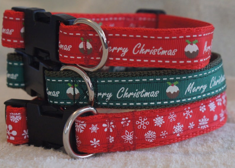 May include: Three dog collars with Christmas designs. The top collar is red with a white "Merry Christmas" message and a green and brown pudding design. The middle collar is green with a white "Merry Christmas" message and a green and brown pudding design. The bottom collar is red with a white snowflake design.
