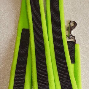 May include: A lime green dog lead with two black stripes running down the length of the lead. The lead has a silver metal clip.