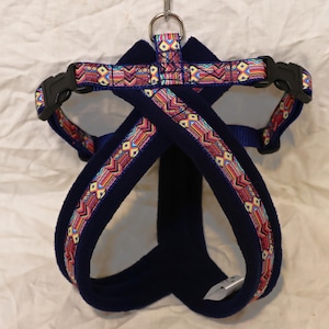 May include: A blue dog harness with a colorful geometric pattern. The harness is made of soft fleece and has adjustable straps.