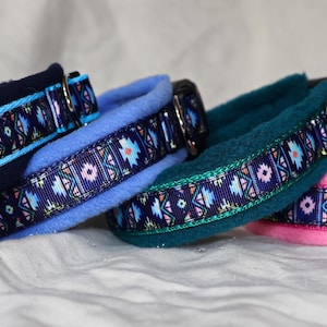 May include: Four dog collars in navy, light blue, teal, and pink. Each collar features a patterned ribbon with geometric designs in blue, pink, and teal. The collars are made of soft, plush material.