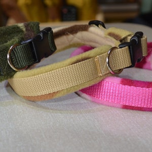 May include: Three dog collars with fleece lining. One is green camouflage, one is tan, and one is pink with a floral pattern.