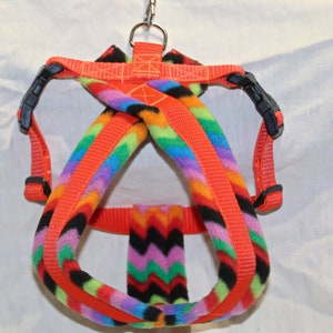 May include: A bright orange dog harness with a colourful, zigzag patterned fleece lining. The harness has a metal clip for attaching a lead.