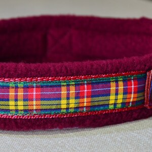 May include: Burgundy fleece dog collar with a plaid ribbon trim. The collar has a silver metal D-ring and a black plastic buckle.