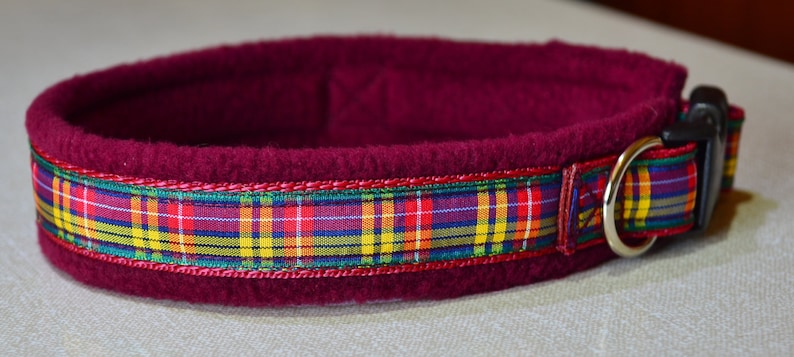 May include: Burgundy fleece dog collar with a plaid ribbon trim. The collar has a silver metal D-ring and a black plastic buckle.