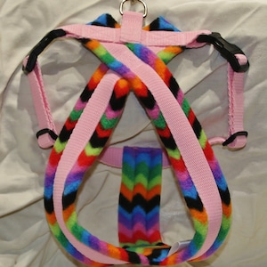 May include: Pink dog harness with a rainbow chevron pattern fleece lining. The harness has a metal D-ring and adjustable straps.