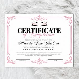 May include: A white certificate with pink decorative borders and text. The certificate reads "CERTIFICATE of Completion" and is awarded to "Miranda Jane Charlston" for completing a lash course. A silver pen is on the left.