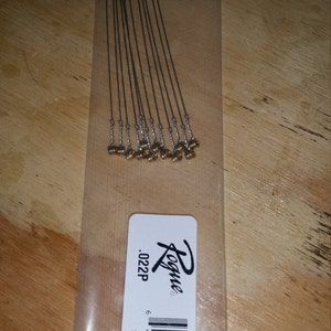 May include: A pack of 12 silver guitar strings with gold-colored ends. The pack is labeled "Rogue .022P #120022".