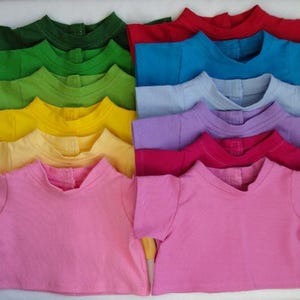 Puede incluir: Una colección de camisetas de manga corta coloridas en varios tonos, incluyendo verde, amarillo, rosa, rojo y azul. Las camisetas están cuidadosamente dispuestas, mostrando una gama de tonos vibrantes. Las camisetas son probablemente para niños o muñecas.